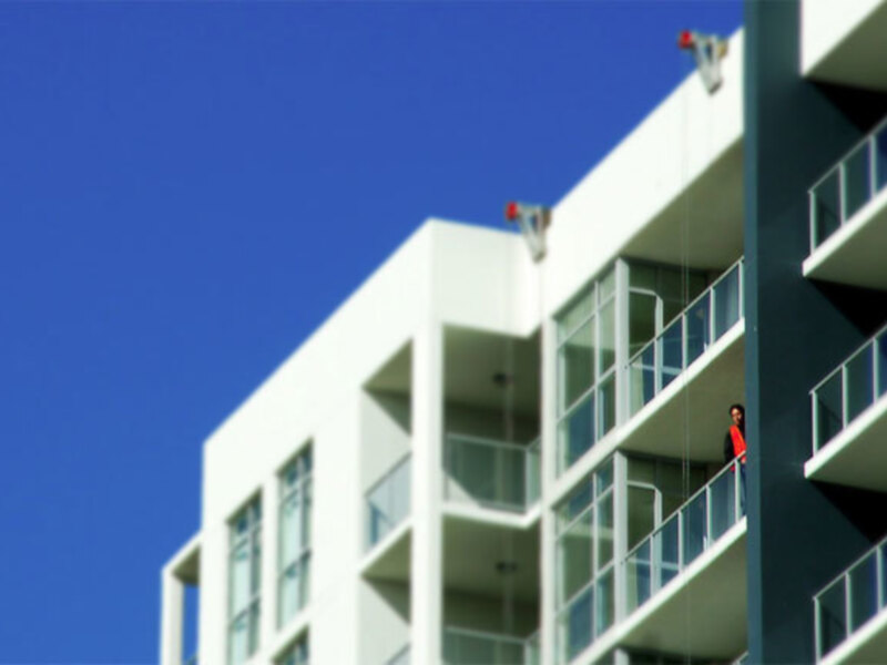 Edificio moderno con balcones y una persona en el balcón superior bajo un cielo azul claro.