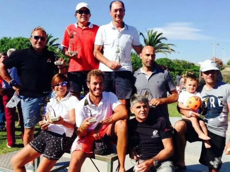Equipo ganador de un torneo de tenis con trofeos y felicitaciones en un parque soleado.