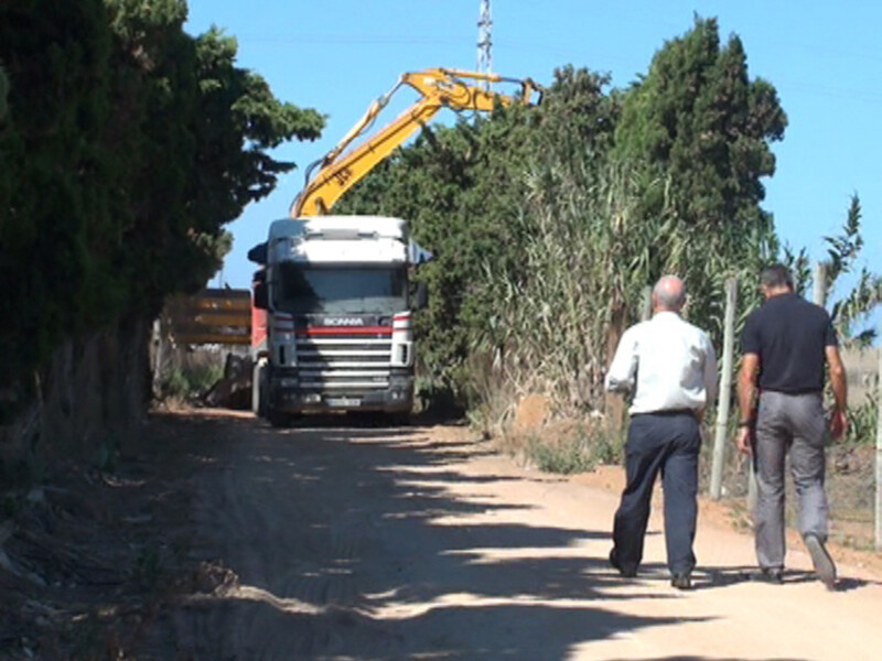 Trabajadores caminando por un camino rural mientras un camión Scania realiza tareas de construcción o mantenimiento.