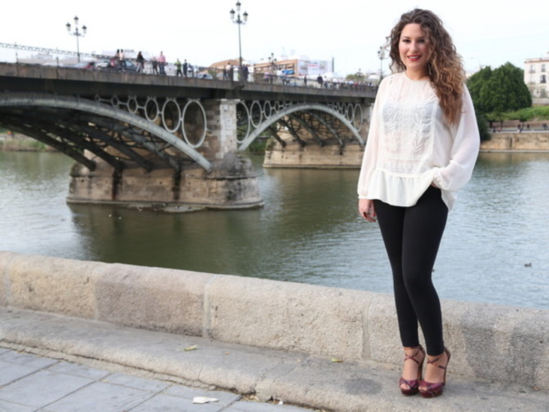 Mujer posando frente al Puente de Triana, Sevilla, con ropa casual y fondo de río y puente.