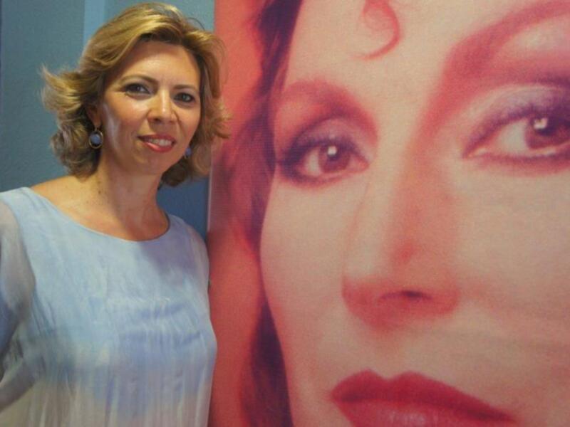 Una mujer sonríe junto a una gran imagen de una cara.