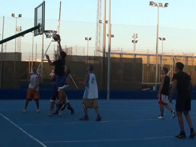 Jugadores de baloncesto en acción durante un partido en una cancha al aire libre al atardecer.