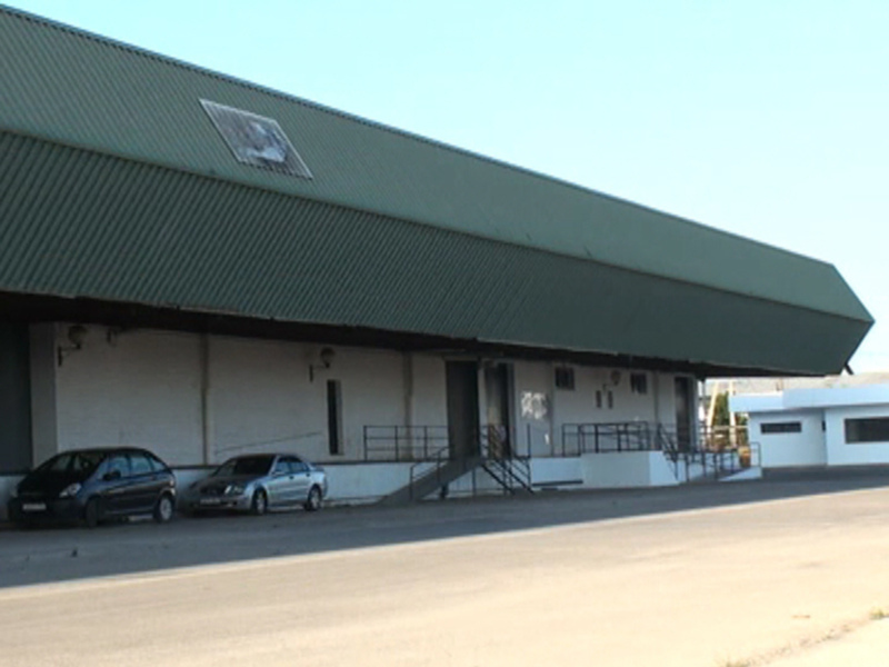 Fachada de un edificio industrial con techo de metal y dos coches estacionados en la entrada.