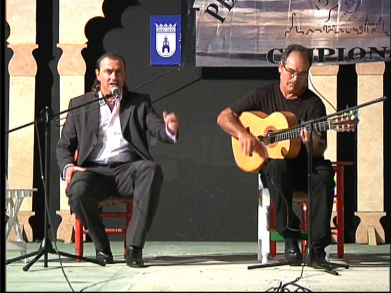 Dos músicos actúan en escenario, uno canta y toca el piano, otro toca la guitarra acústica.