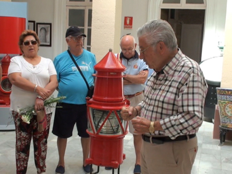 Un grupo de personas examina un faro rojo en un entorno interior, posiblemente en un museo o exposición.