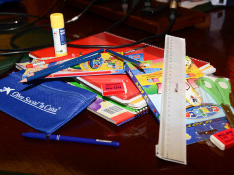 Un escritorio con un bolígrafo azul, un lápiz negro, un estuche de lápices, un marcador amarillo, un lápiz de colores y un cuaderno azul con la marca 'Ober Sociale La Citta'.