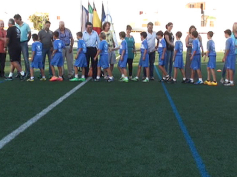 Niños jugando fútbol en un campo de fútbol con jugadores y entrenadores observando la acción.