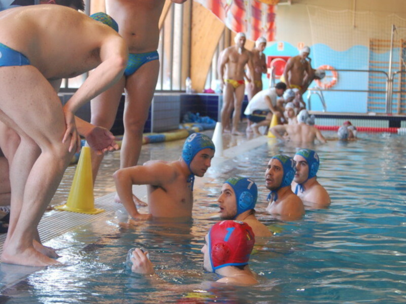 Jóvenes jugadores de waterpolo en una piscina, con los cascos azules y los trajes de baño azules, preparándose para el partido.