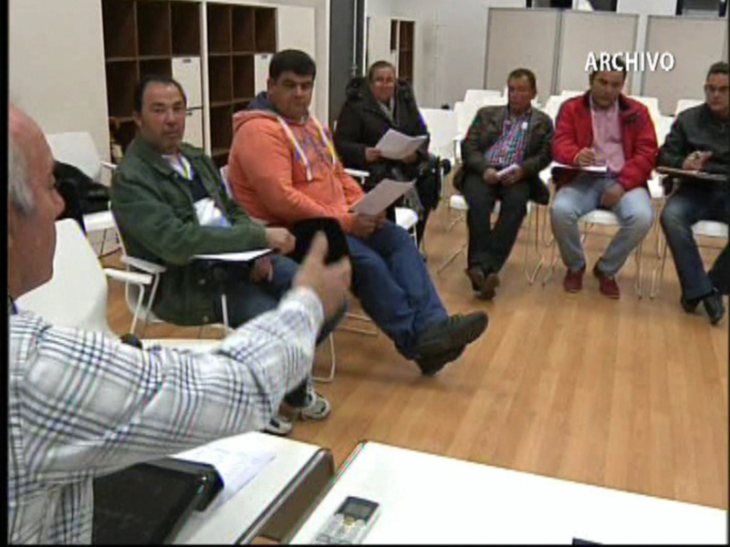 Reunión de trabajo en una sala de reuniones con participantes sentados en sillas y un moderador en el centro.