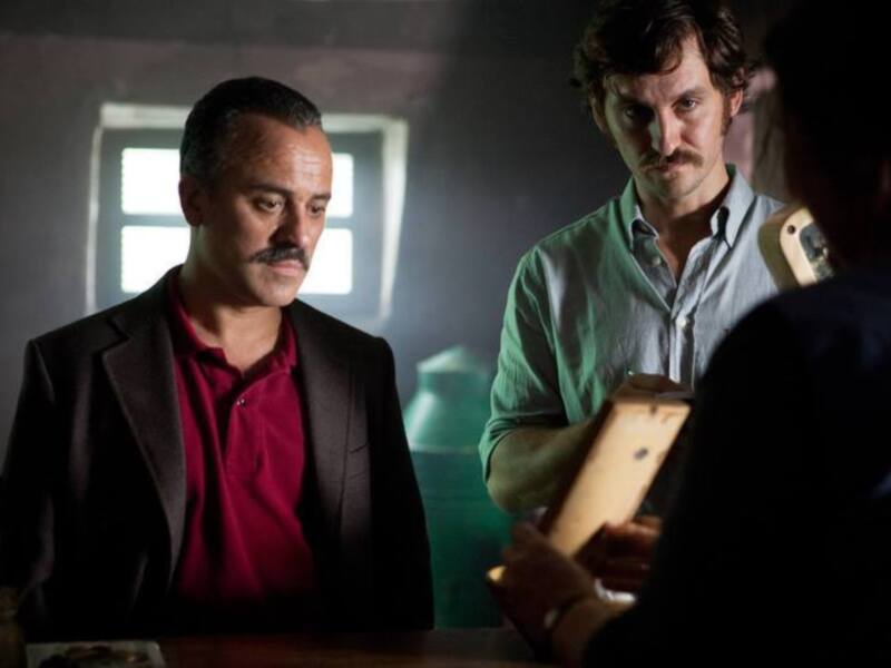 Dos hombres en una escena de filmación, uno con una camisa roja y el otro con una camisa verde, ambos mirando hacia la derecha.