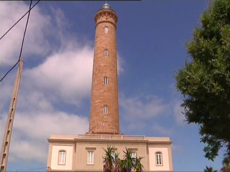 Altura monumental del Faro de Chipiona bajo un cielo azul con nubes.