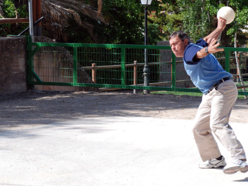 Un hombre juega a la petanca en un parque soleado.