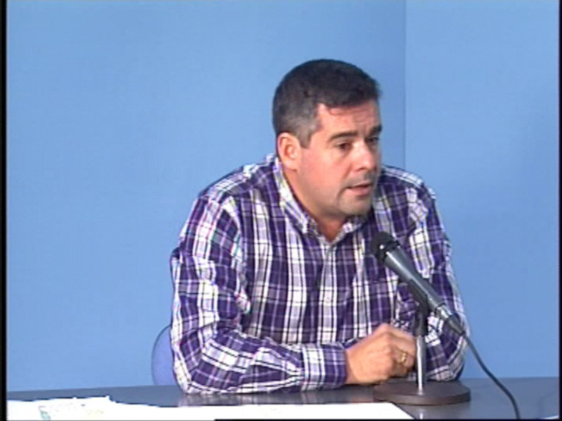 Hombre hablando en una conferencia con micrófono y fondo azul claro.