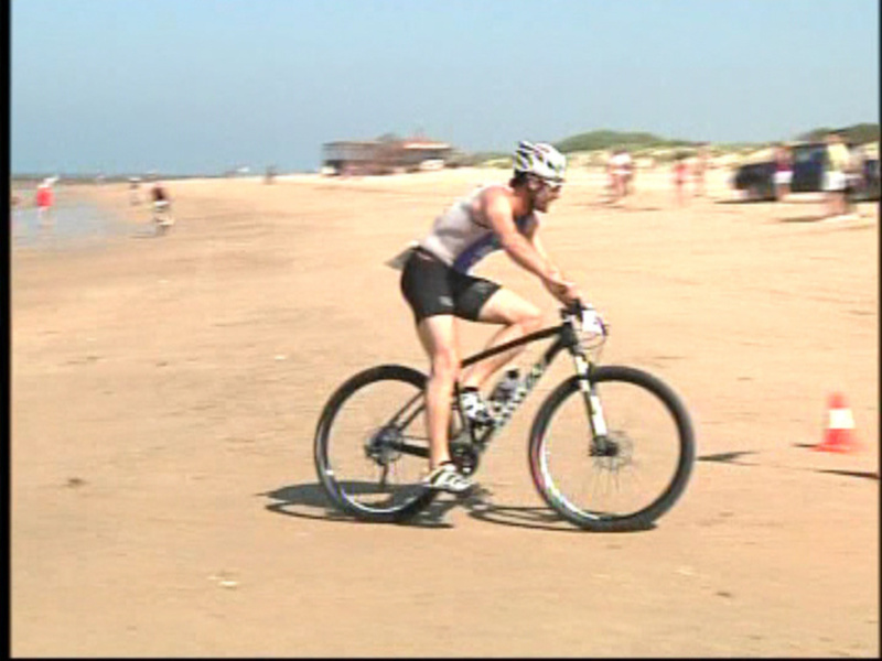 Atleta en bicicleta durante una competición en la playa.