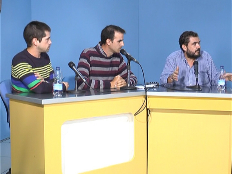 Tres personas sentadas detrás de una mesa con micrófonos, probablemente en una reunión o debate.