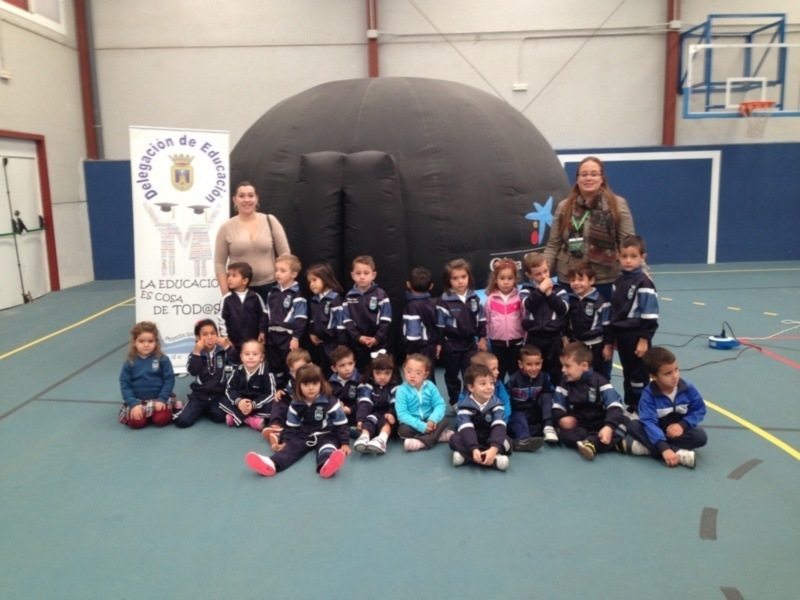 Niños y niñas de una escuela infantil posando para una foto en una cancha de baloncesto, con una bola gigante inflable en el fondo.