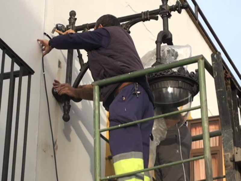 Trabajador reparando una lámpara de calle en una pared exterior.