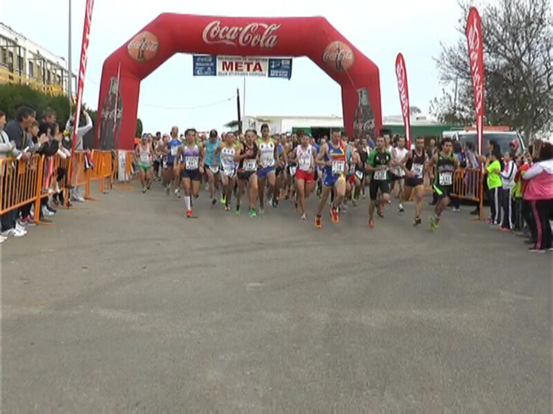 Corredores participando en una carrera de larga distancia bajo la arco de meta de Coca-Cola.