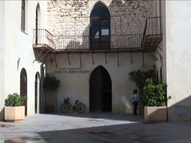 Edificio histórico con arco gótico y balcones, en un entorno urbano con una persona caminando.