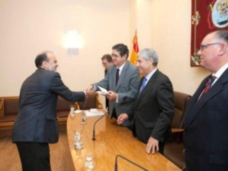 Reunión formal en un entorno institucional, con hombres vestidos de traje intercambiando documentos.
