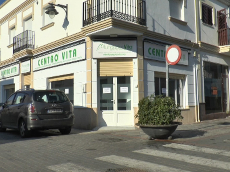 Centro de atención a la salud en una calle de la ciudad, con dos vehículos estacionados y una planta en el frente de la tienda.