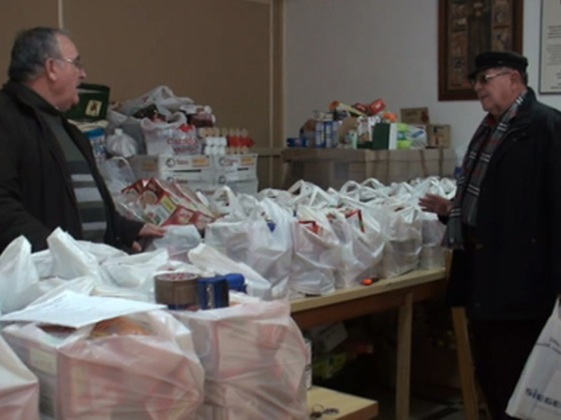 Dos personas conversando en un almacén lleno de cajas y bolsas de alimentos, probablemente en una escena de distribución de alimentos.