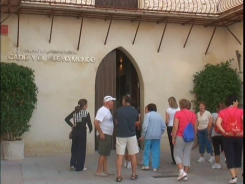 Un grupo de personas esperando en fila frente a una entrada de un edificio con una placa que dice 'Centro de Interpretación del Nuevo Mundo'.