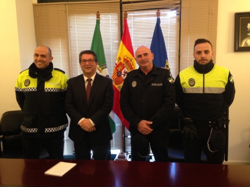 Tres personas, dos de ellas con uniformes de policía, posan frente a banderas de Portugal y España en una oficina formal.