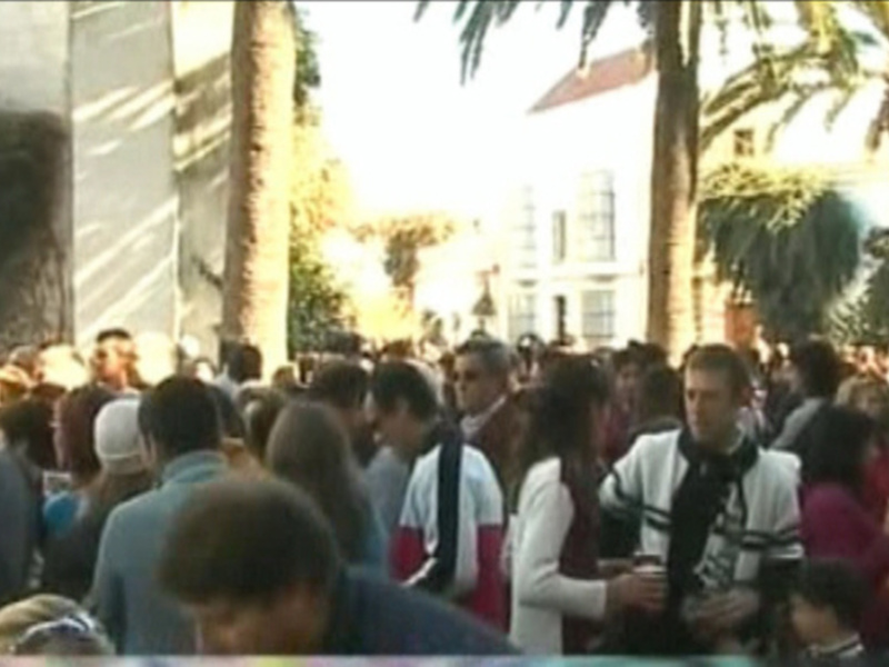 Calle con gente en una ciudad, árboles y edificios al fondo.