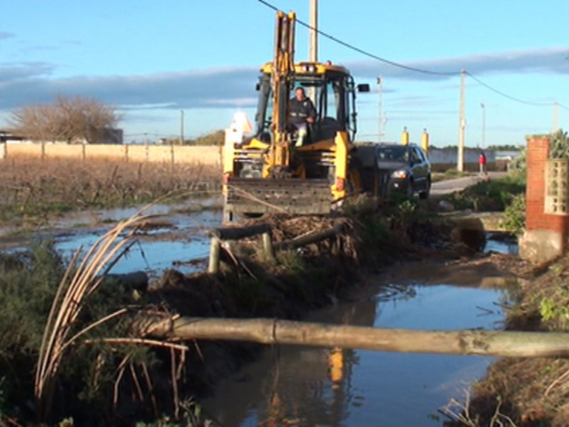 Tractor trabajando en una zona inundada cerca de una carretera rural.