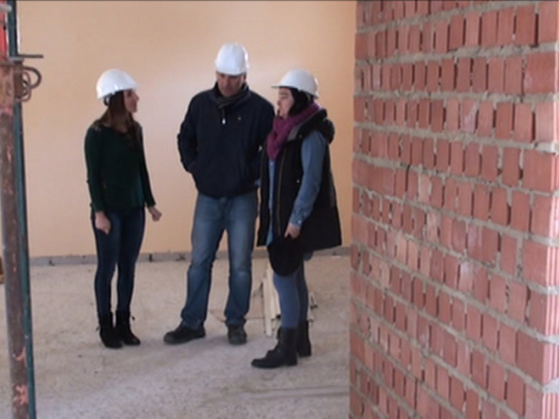 Tres personas en cascos de construcción conversando en una obra en construcción.