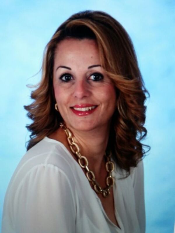 Retrato de mujer sonriente con cabello ondulado y collar dorado, fondo azul claro.