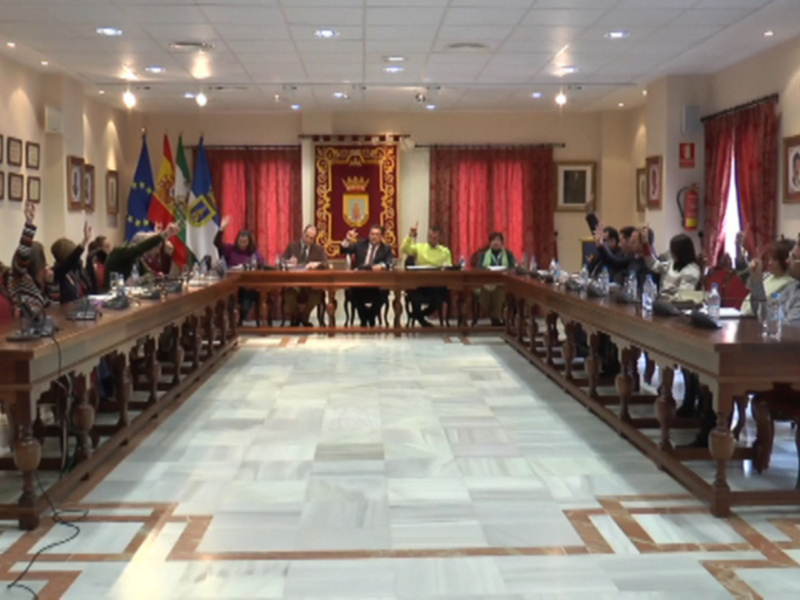 Reunión de consejo municipal en una sala con banderas y mesas de discusión.