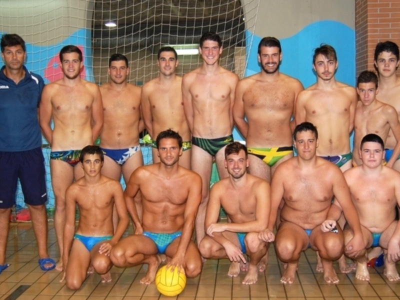 Equipo de waterpolo masculino en una piscina, con entrenador y jugadores en traje de baño, posando con un balón de waterpolo.