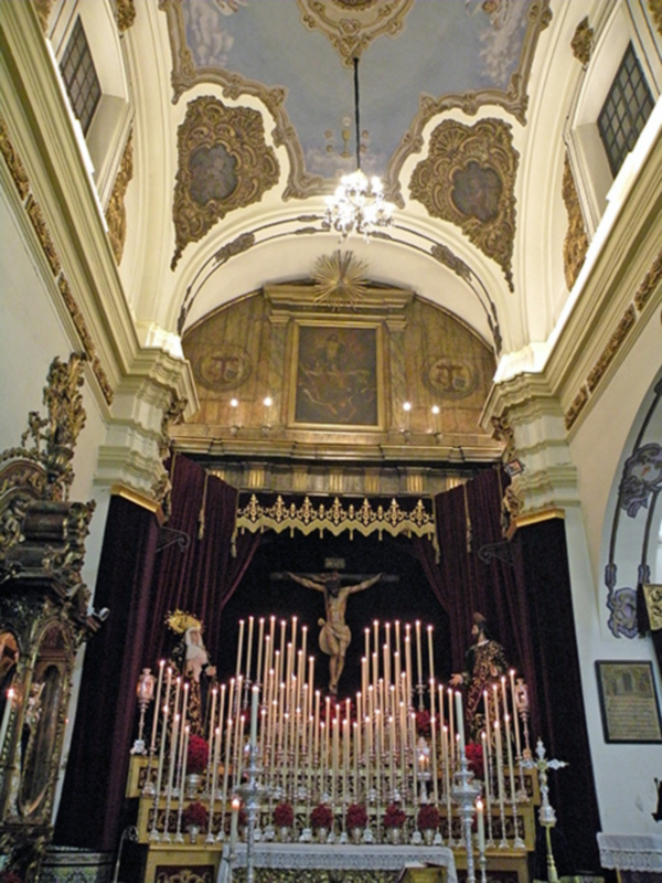 Interior de una iglesia con altares y candelabros encendidos, iluminando la atmósfera sagrada y solemn.