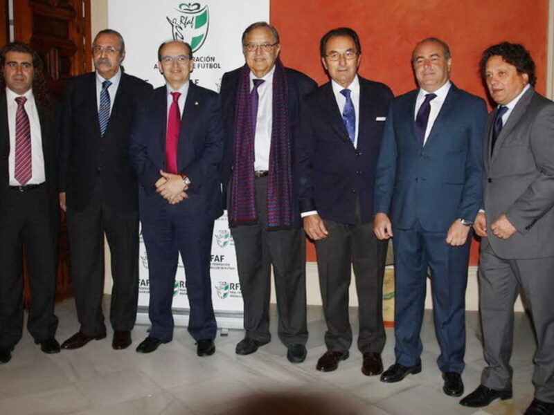Grupo de hombres en trajes posando frente a un cartel con el logo de la Real Federación Española de Fútbol.