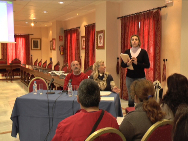 Jornada de formación en sala decorada con cortinas rojas, presentación en pantalla y participación activa del público.