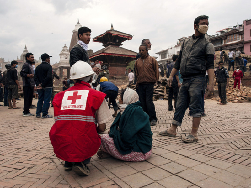 Voluntarios de la Cruz Roja de Nepal asisten a personas afectadas por un terremoto en una plaza histórica.