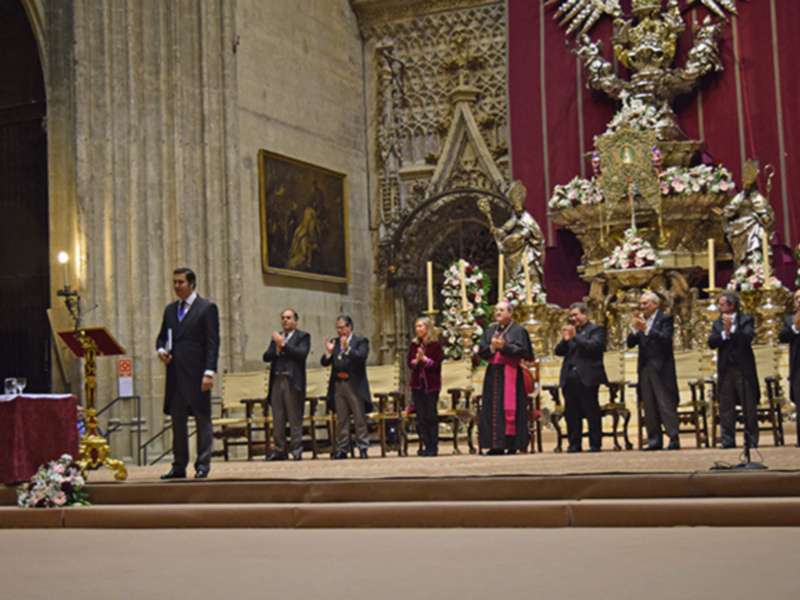 Celebración en una catedral con personas en trajes formales y un altar adornado con flores y velas.