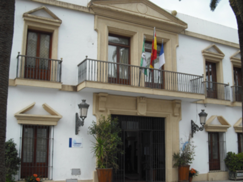 Fachada de un edificio blanco con balcones y banderas, típico de la arquitectura andaluza.