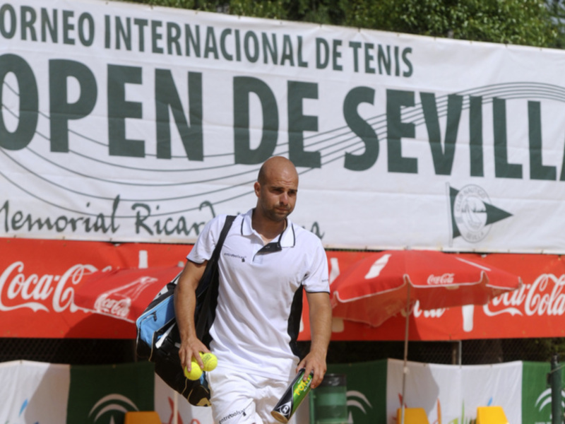Jugador de tenis en el Open de Sevilla, con cartelera del torneo y publicidad de Coca-Cola en el fondo.