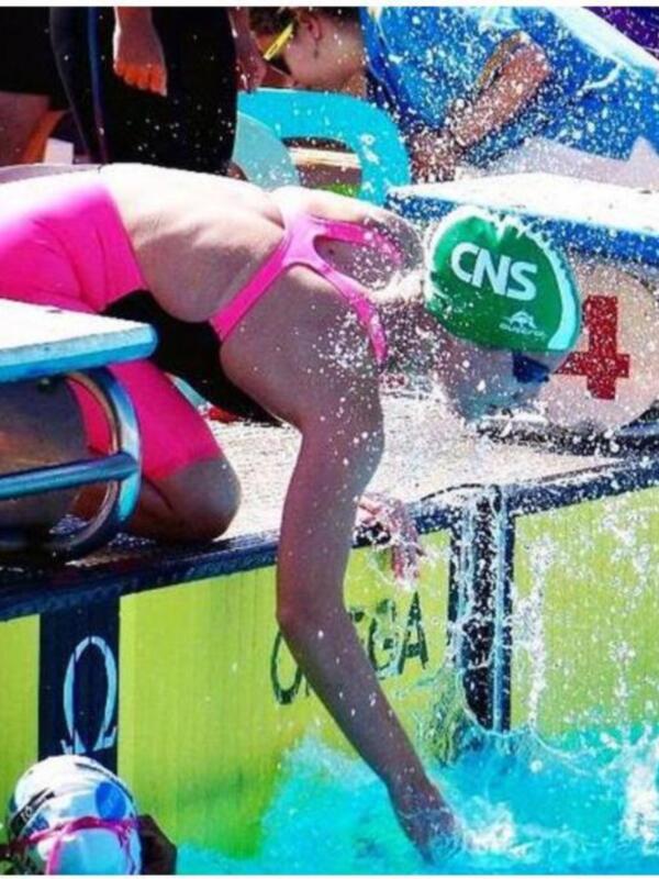 Niña nadando en una piscina con un traje de baño rosa y una gorra azul. La piscina tiene un diseño con letras y números en el fondo.