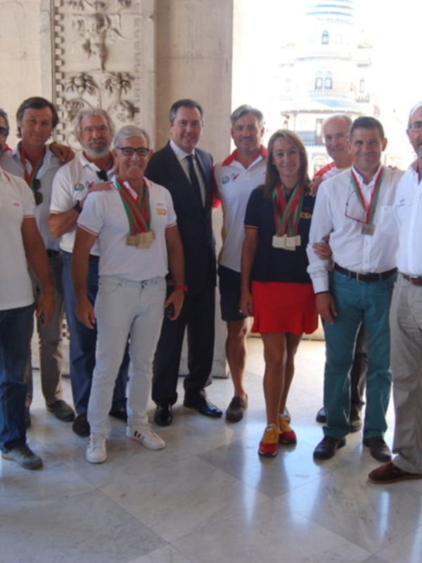 Una reunión formal en un edificio histórico, con varios hombres y una mujer posando para la foto, algunos llevando medallas de oro. El ambiente es formal, con vestimenta elegante y un fondo que incluye elementos arquitectónicos antiguos.