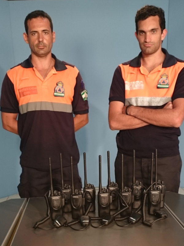 Dos miembros de Protección Civil con uniformes y radios de comunicación en una mesa.