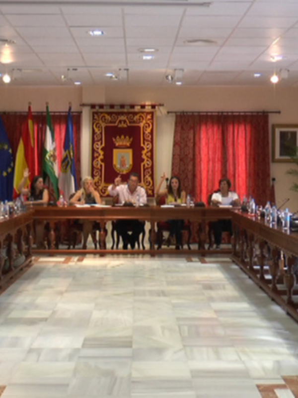 Reunión en sala de conferencias con banderas y escudo de armas en el fondo.