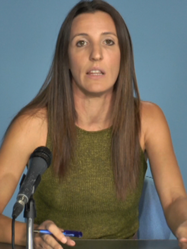 Persona hablando en una conferencia de prensa con un micrófono y un fondo azul.