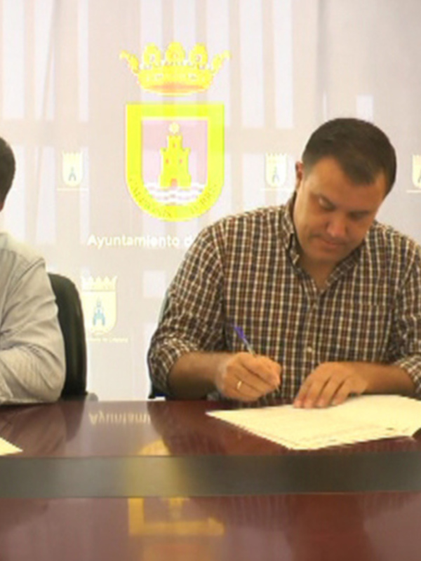 Tres personas firmando documentos en una sala con el escudo del Ayuntamiento de Algeciras en el fondo.