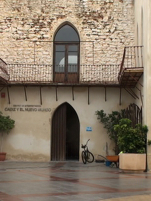 Fachada antigua de un edificio con arcos góticos y balcones en un patio con plantas y bicicleta.