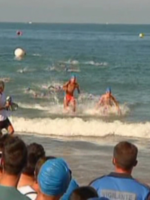 Competidores en una carrera de natación en el mar, rodeados por espectadores en la playa.
