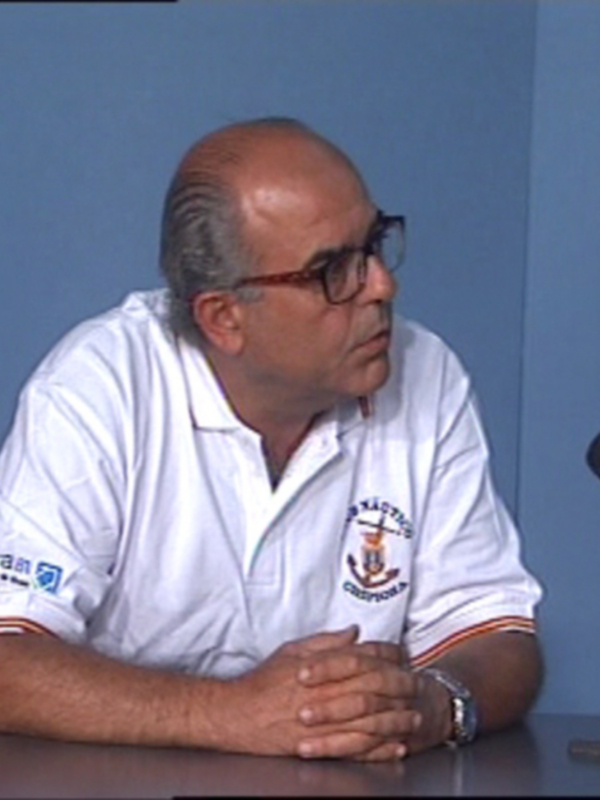 Persona en una conferencia de prensa, sentado en una mesa con un micrófono frente a él.
